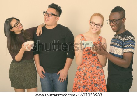 Studio shot of happy diverse group of multi ethnic friends smiling while using mobile phone together with friends having coffee in the back