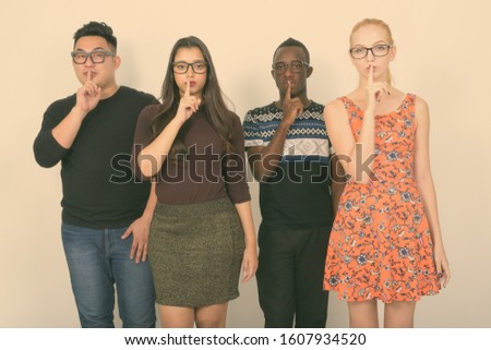 Studio shot of diverse group of multi ethnic friends with finger on lips while wearing eyeglasses together
