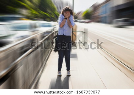 Lady having a panic attack outside in public space holding her hands on her face. Scared person feeling despair on a sidewalk. Anxiety issues or mental problems concept Royalty-Free Stock Photo #1607939077