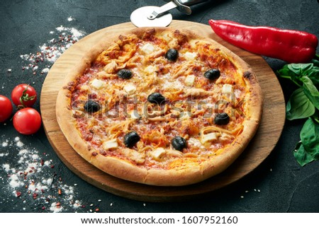 Pizza with a large number of toppings: chicken, onions, mushrooms, olive. Pizza in composition with ingredients on a black background