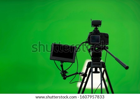 Camera on tripod connected with monitor on green screen background.