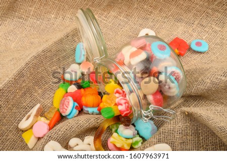 Multicolored shaped marmalade in a glass jar on a background of rough homespun fabric close-up. Delicious holiday treat.
