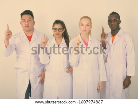 Studio shot of diverse group of multi ethnic doctors pointing finger up together