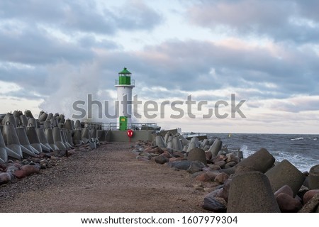 Windy winter with high waves and lighthouse and breakwater in Baltic sea near the port of Ventspils.