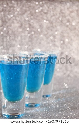 Three glasses with blue alcoholic drinks. Stand on a silver shiny background.