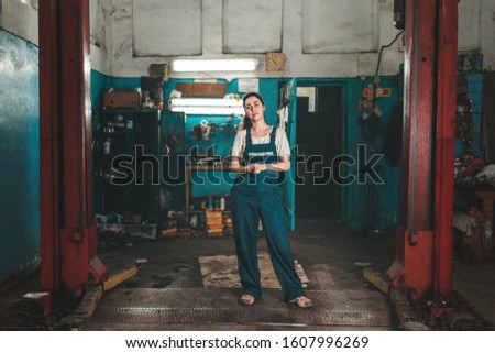Gender equality. A young brunette woman in uniform, standing against the background of a car repair shop. Horizontal