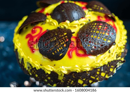 Sponge cake smeared with yellow butter cream and decorated with chocolate figures. On a blue tablecloth and a blue background