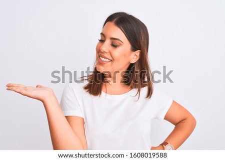 Portrait of beautiful and young brunette woman standing over isolated white background smiling cheerful presenting and pointing with palm of hand looking at the camera.