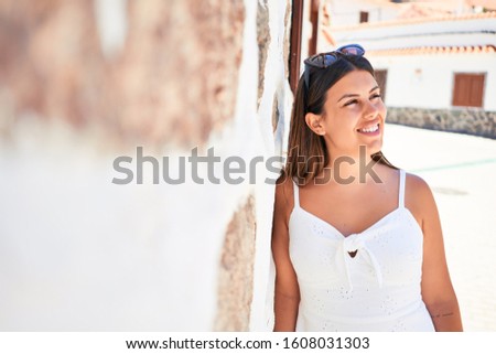 Beautiful girl leaning on white wall, young friendly woman smiling happy on a sunny day of summer