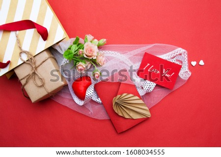 From a gift bag flat lay a gift, an envelope, a heart, flowers and tulle with I love you text on a card. Valentine's Day concept
