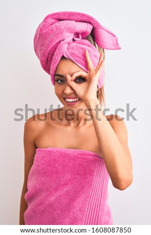 Young beautiful woman wearing shower towel after bath over isolated white background with happy face smiling doing ok sign with hand on eye looking through fingers