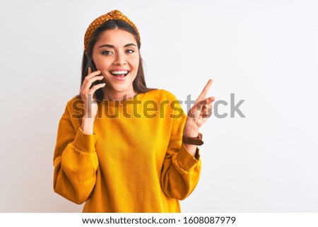 Young beautiful woman talking on the smartphone standing over isolated white background very happy pointing with hand and finger to the side