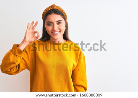 Young beautiful woman wearing yellow sweater and diadem over isolated white background smiling positive doing ok sign with hand and fingers. Successful expression.