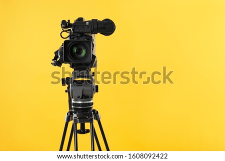Modern professional video camera on yellow background. Space for text