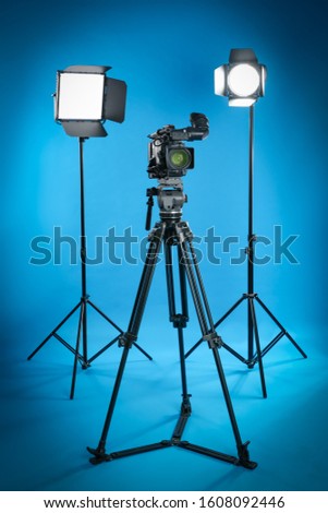 Professional video camera and lighting equipment on blue background