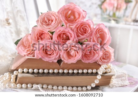 vintage style picture with bunch of pink roses and pearls lying on old books