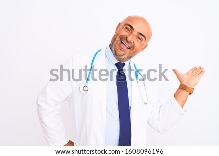 Middle age doctor man wearing stethoscope and tie standing over isolated white background smiling cheerful presenting and pointing with palm of hand looking at the camera.