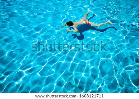 Unrecognizable young man doing an underwater breast stroke in a bright blue swimming pool