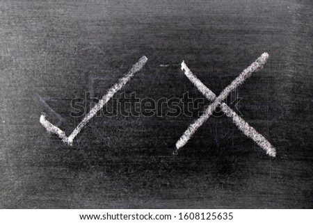 White color chalk hand drawing as check mark of right and wrong shape on black board background