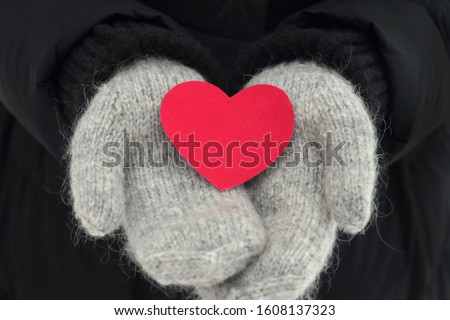 Red heart in hands on black backgroind. Gray mittens. Stock photography fo valentine's day. Winter mood 