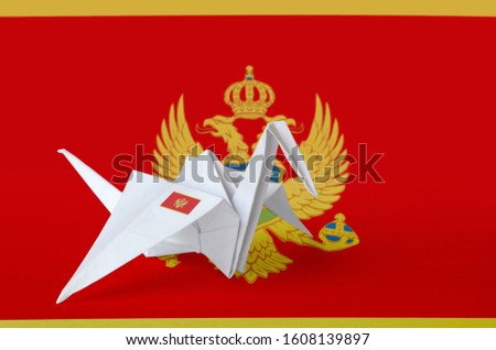 Montenegro flag depicted on paper origami crane wing. Handmade arts concept