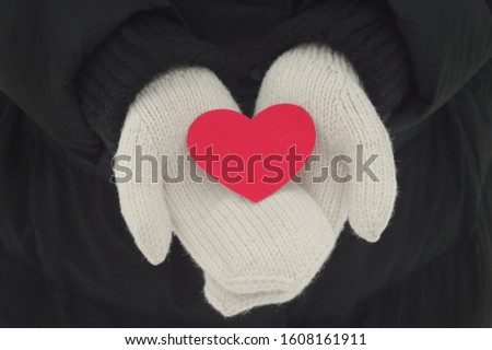 Red heart in hands on black backgroind. Wite mittens. Stock photography fo valentine's day. Winter mood 
