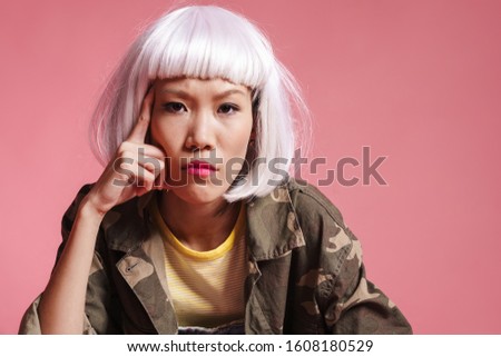 Image of frustrated asian girl wearing white wig thinking and looking at camera isolated over pink background