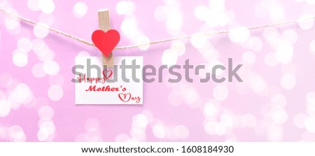Happy Mother's Day background banner panorama - White paper note hang on wooden clothes pegs with wooden hearts on a string isolated on pink paper texture and bokeh lights, with space for text
