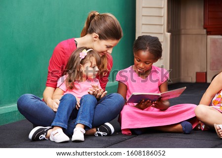 African girl reads book in kindergarten next to kindergarten teacher