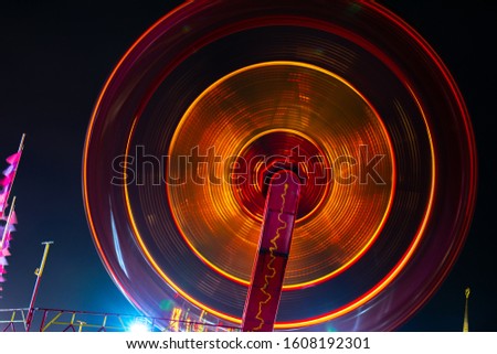 Photo of a carousel at night in a long exposure in an amusement park. The yellow and redder tones of the carousel bulbs merge in motion and give the image a glowing disk effect.