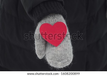 Red heart in hands on black backgroind. Gray mittens. Stock photography fo valentine's day. Winter mood 