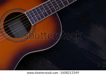 Cropped image of vintage style travel size acoustic guitar with rosewood neck and no pickguard on grunged dark wood textured background. Close up, copy space for text, top view.