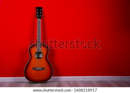 Cropped image of vintage style travel size acoustic guitar with rosewood neck and no pickguard over festive red wall background. Close up, copy space for text, top view.