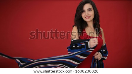 portrait of a beautiful girl with dark hair in a striped dress on a red background in a good positive mood, a young woman free space for notes