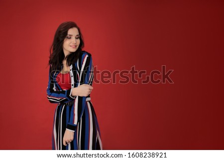 portrait of a beautiful girl with dark hair in a striped dress on a red background in a good positive mood, a young woman free space for notes