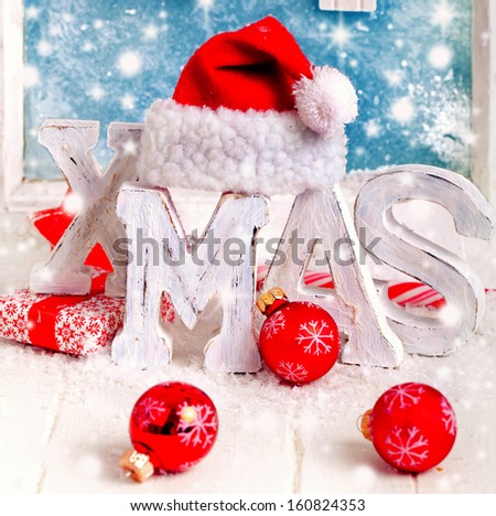 xmas letters with red santa claus hat and red christmas balls with blue window in background