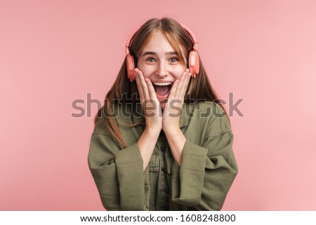 Photo of excited caucasian woman using headphones and smiling isolated over pink background