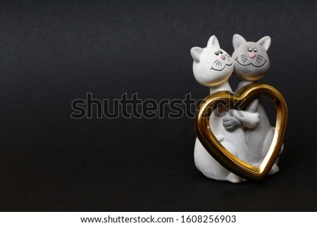 Two cats are hugging. Cats are close and love each other. Valentines Day. Figurine cats in love. Nearby is a golden heart. Cats together are a symbol of lovers. Congratulation.