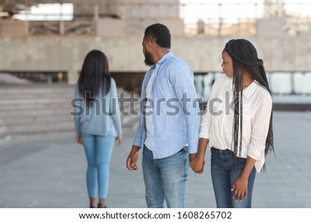 Infidelity concept. Black millennial guy distracted to another woman while walking with his girlfriend in city, selective focus Royalty-Free Stock Photo #1608265702