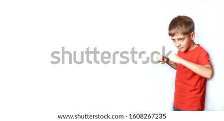 Close-up Portrait of a young cute attractive boy, a teenager in a red t-shirt. He clenches his fingers into fists and glares at the camera.  Isolated white background, banner, copy space.