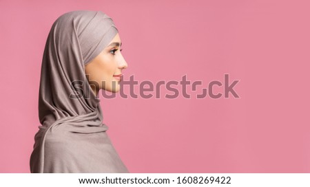 Muslim Beauty. Profile portrait of modest islamic girl in hijab looking at copy space over pink background, panorama Royalty-Free Stock Photo #1608269422