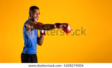 Ready For Fight. Aggressive black man practicing boxing punches in gloves, yellow background. Panorama, copyspace