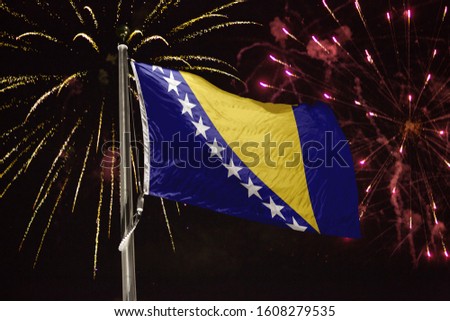 Bosnia and Herzegovina flag blowing in the wind at night with fireworks