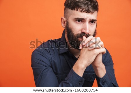 Image closeup of uptight man with nose jewelry wearing black shirt thinking with fists clenched isolated over orange background Royalty-Free Stock Photo #1608288754