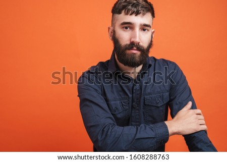 Image closeup of serious man with nose jewelry wearing black shirt looking at camera isolated over orange background
