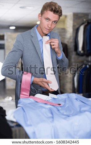 Man buyer in shirt choosing colored tie in the dress shop