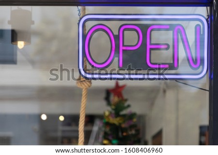 purple neon light hang from ceiling with clear glass of restaurant. open sign of coffee shop on daytime.