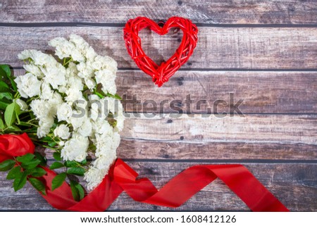 A bouquet of white roses with a red ribbon and rattan heart on a background of dark boards. Valentine's day, wedding, declaration of love. Place for text, top view, Copy space, Flat Lay.