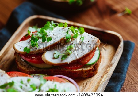 Sandwiches with turkey meat and fresh vegetables served with microgreens on a wooden plate
