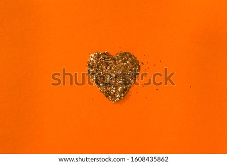 Golden sparkles heart shaped on vivid orange background, top view, selective focus. Festive minimal concept.